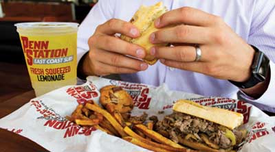 man eating a cheesesteak and fries